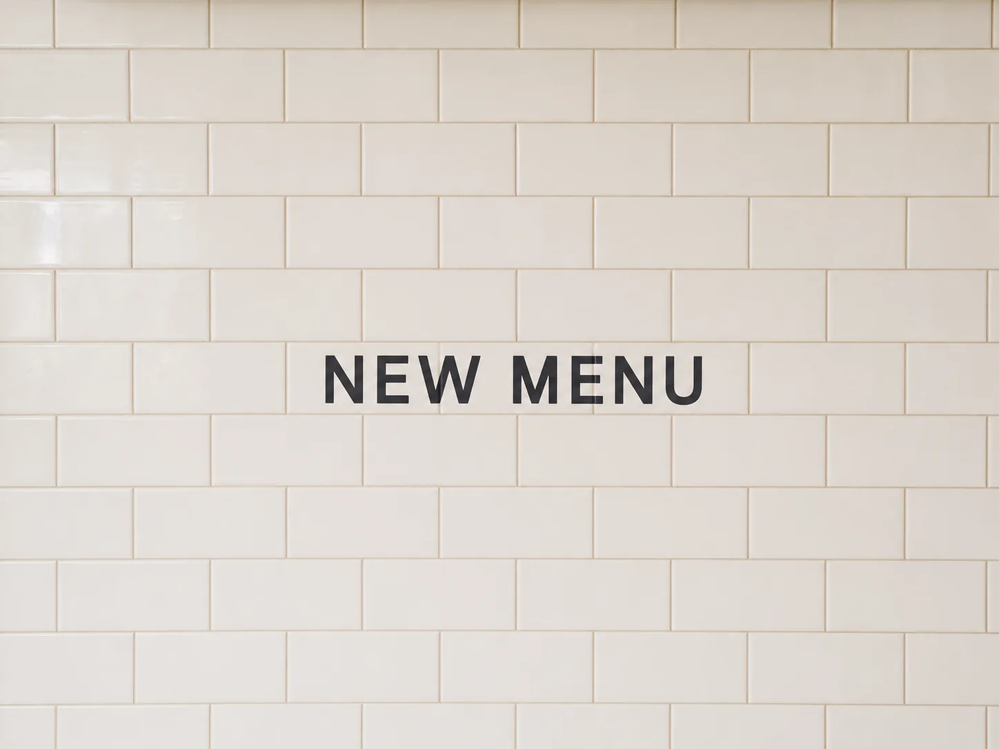Recommended example with the short words NEW MENU centered on a broad repeating cream tile wall